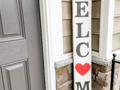 welcome sign with heart as O next to door on front porch