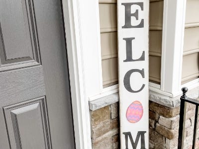 welcome sign with egg as O next to door on front porch