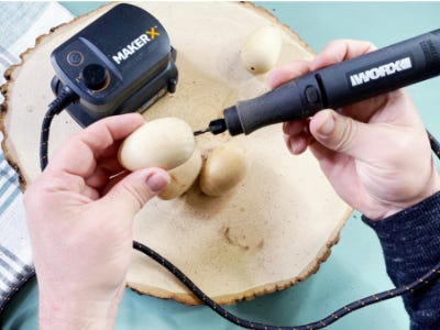 Rotary tool drilling into bottom of egg with eggs behind on wooden plate