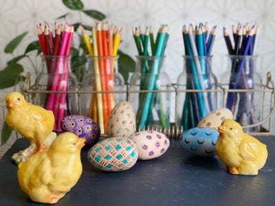 Colorful eggs in front of multi color pencils with yello chickens