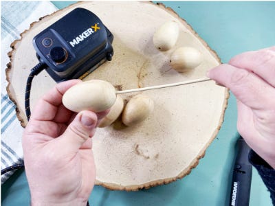 Poking stick into bottom of egg with eggs behind on wooden plate