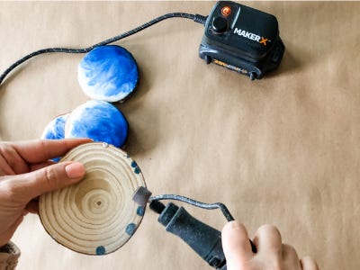 Rotary tool sanding down the edges of wood coaster thats flipped upside down