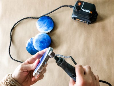 Rotary tool sanding down the edges of wood coaster thats on the side