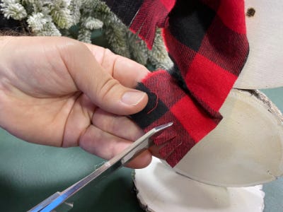 using scissors to cut red and black plaid scarf