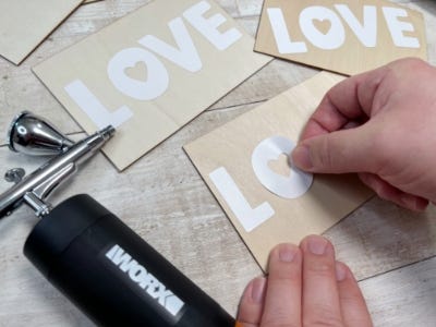 person placing on the precut letter sticks to spell love on a blank card with the makerx air brush laying to their left