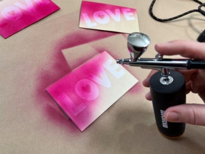 person using the makerx air brush to spray the card the color bright pink