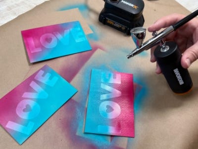 person using the makerx air brush to paint half of the card blue