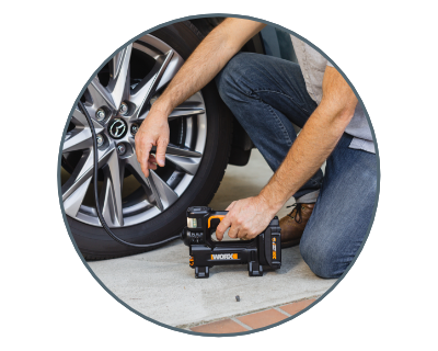 close up of a man kneeling on the ground using the inflator to inflate the tire of a car