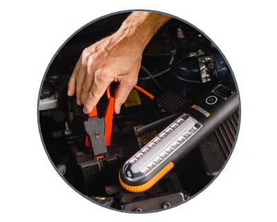 close up of a person attaching jumper cables to a battery with the jumpstarter laying next to it