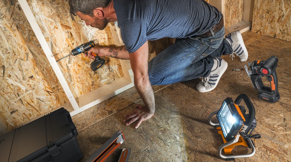 man kneeling and using the drill to attach a beam to to flakeboard