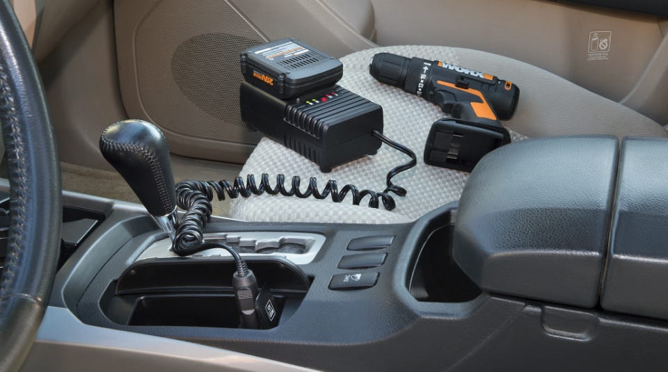 interior car center console with charger plugged into the lighter slot and a battery and drill laying next to on the seat