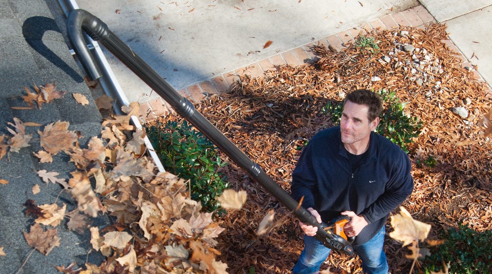 man using the assembled kit to clean the leaves out of the gutters on the side of the house