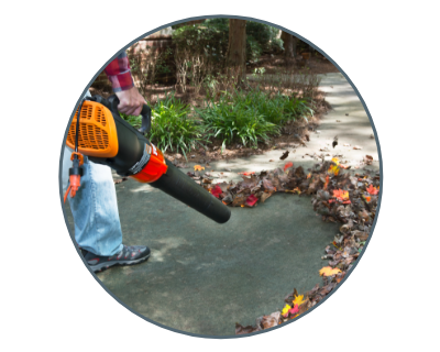 person using the blower to clear leaves from a driveway