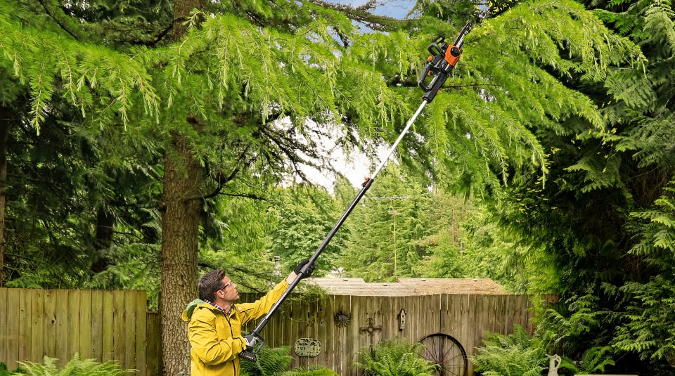 image of a man in a yellow jacket using the worx pole saw to cut limbs from a tree