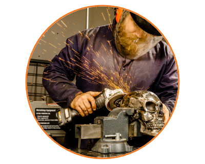 man wearing a mask and gloves using the grinder on a metal skull