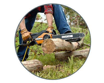 a person hands holding a chainsaw cutting into wood  with one foot holding the wood in place. in a grass field