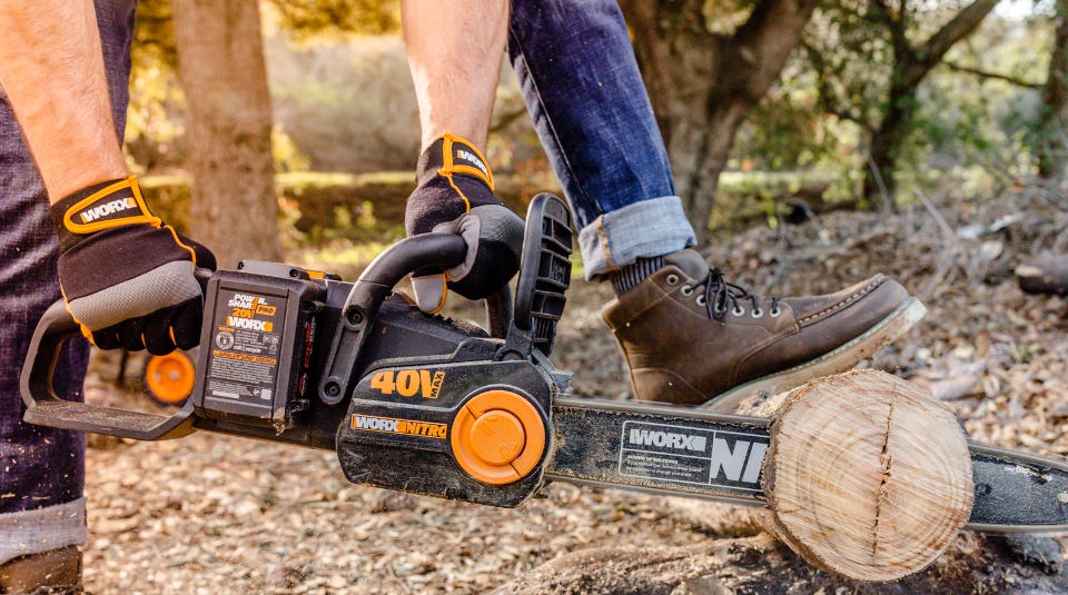 image of a person wearing the gloves while cutting a tree log with a worx chainsaw