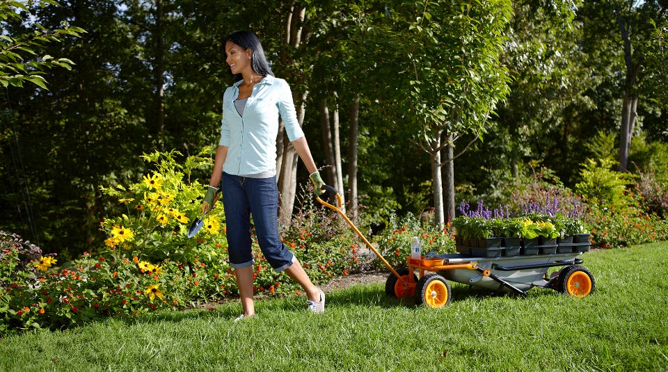 woman pulling the aerocart with the wagon attachment pulling potted flowers she is going to plant in a garden