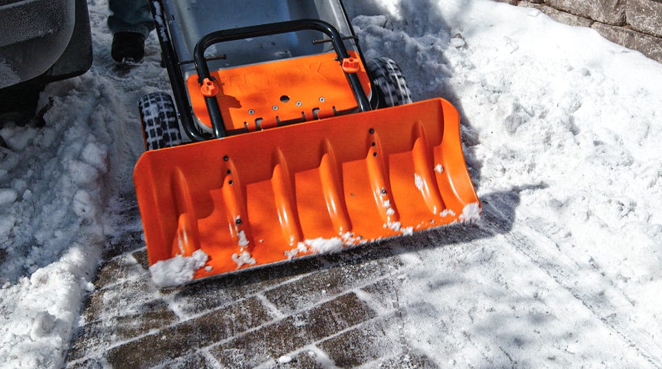 person using the shovel attached to the aerocart to plow the snow from a brick sidewalk